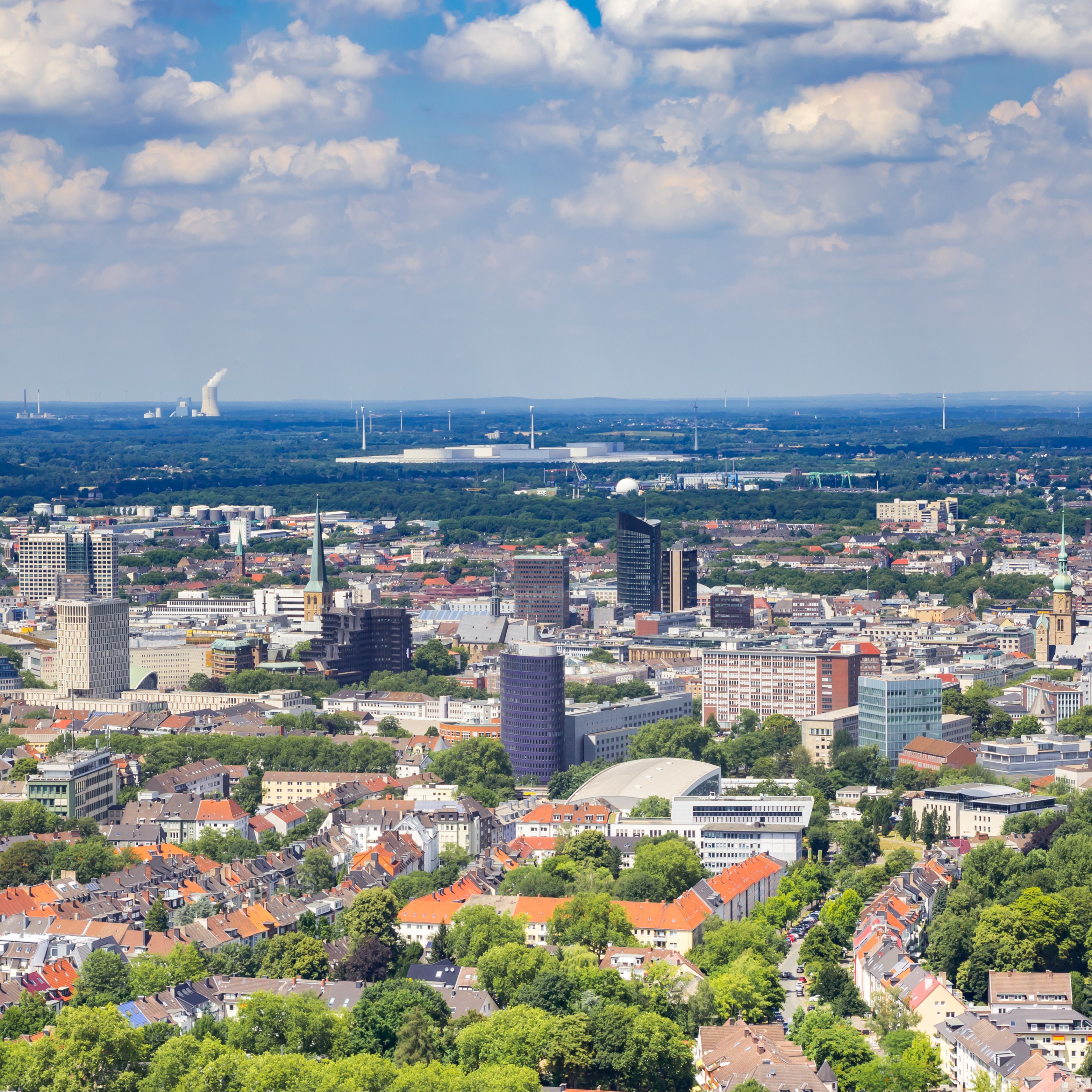 Stadtansicht mit vielen Gebäuden, Bäumen und blauem Himmel mit Wolken.