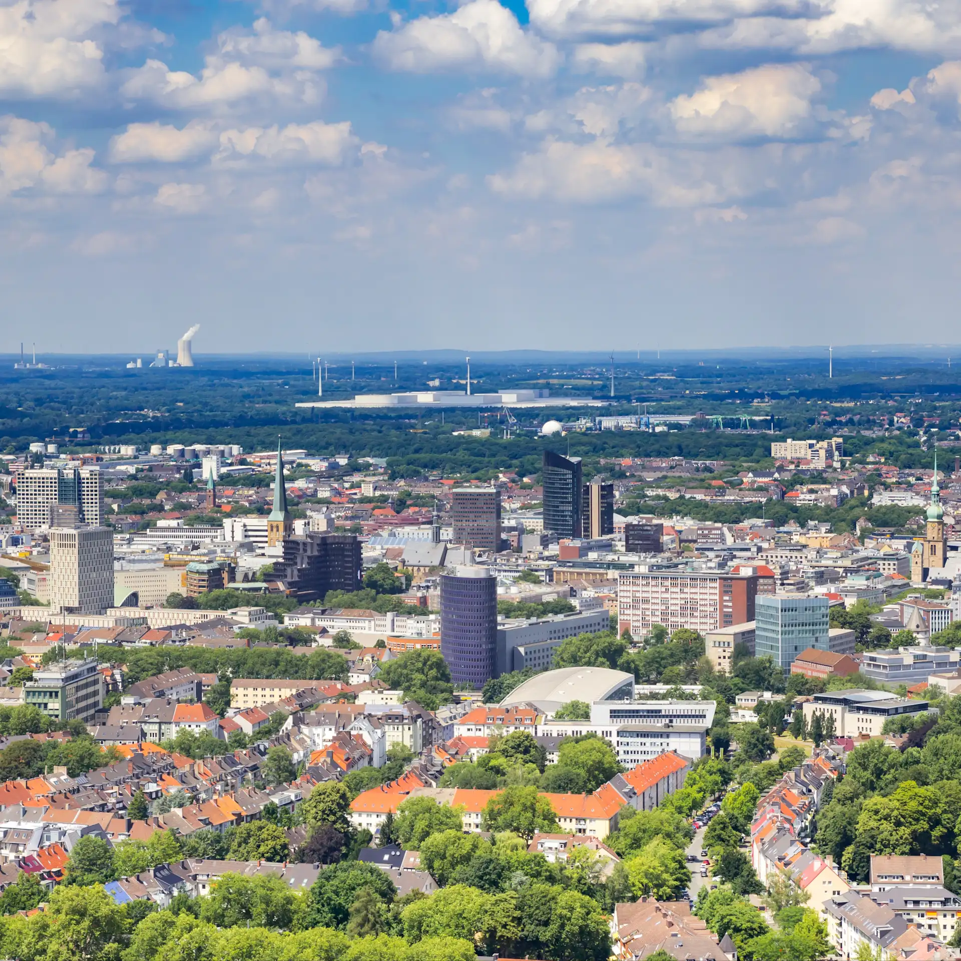 Stadtansicht mit vielen Gebäuden, Bäumen und blauem Himmel mit Wolken.