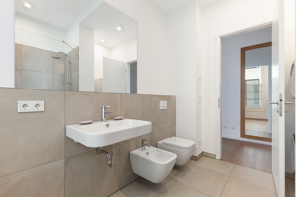 Modernes Bad mit Wandwaschbecken, Bidet und Toilette, großem Spiegel und Fliesenboden.