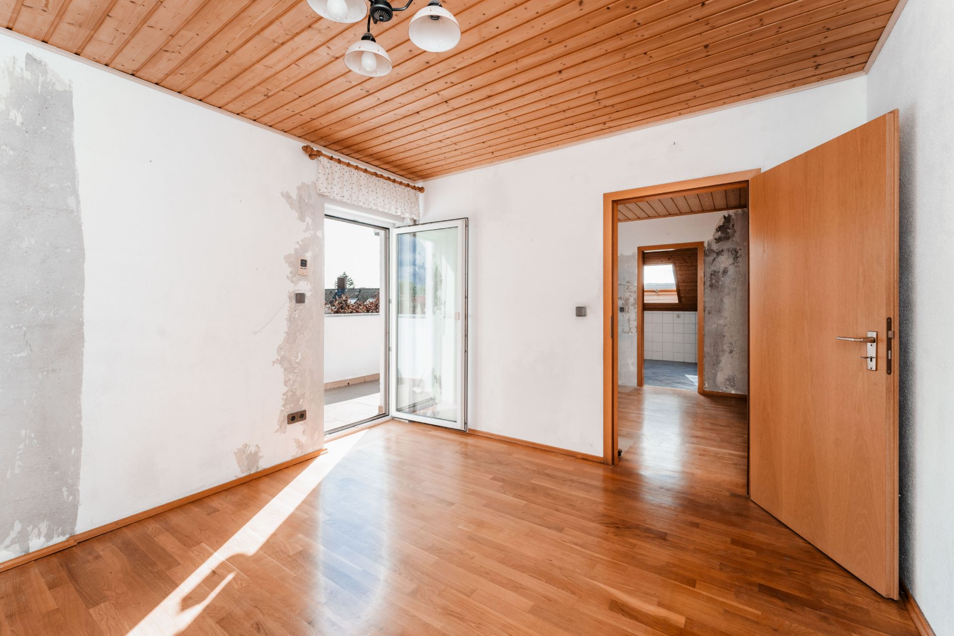 Leerer Raum mit Holzboden, Holzdecke, offener Tür und Zugang zu einem Balkon.