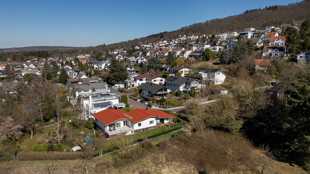 Luftaufnahme eines Wohngebiets mit einzelnen Häusern und Gärten am Waldrand.