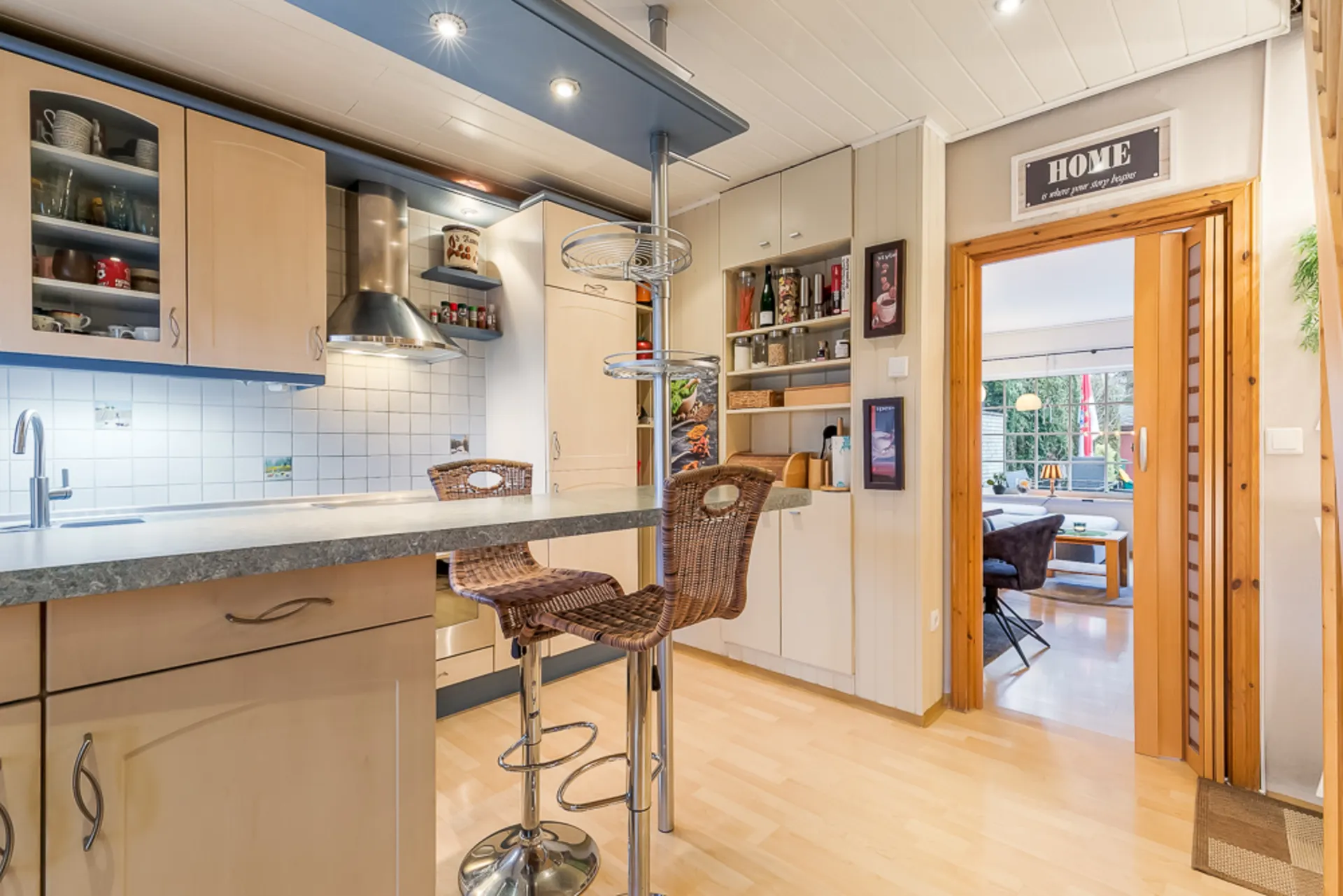 Moderne Küche mit Theke und zwei Barhockern, Blick ins Wohnzimmer mit großem Fenster.