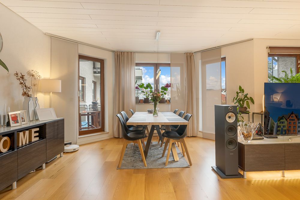 Helles Wohnzimmer mit Esstisch, sechs Stühlen, Sideboard, Pflanzen und großem Fenster.