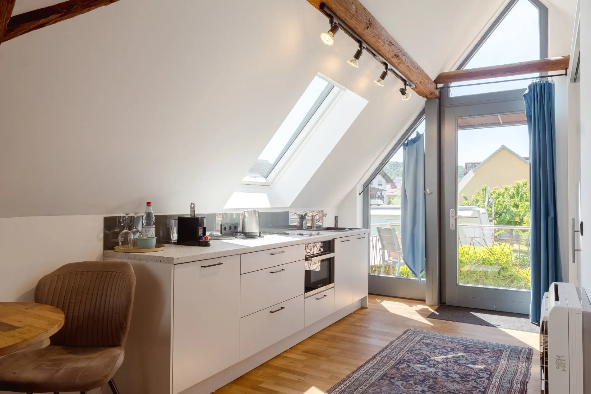 Helle Küche mit Dachschräge, Esstisch, Fensterfront und Zugang zum Balkon.