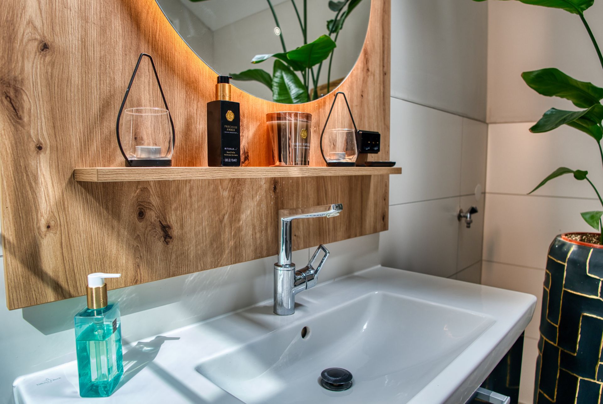 Waschbecken mit Holzspiegel, Pflanzen und Seifenspender im modernen Badezimmer.