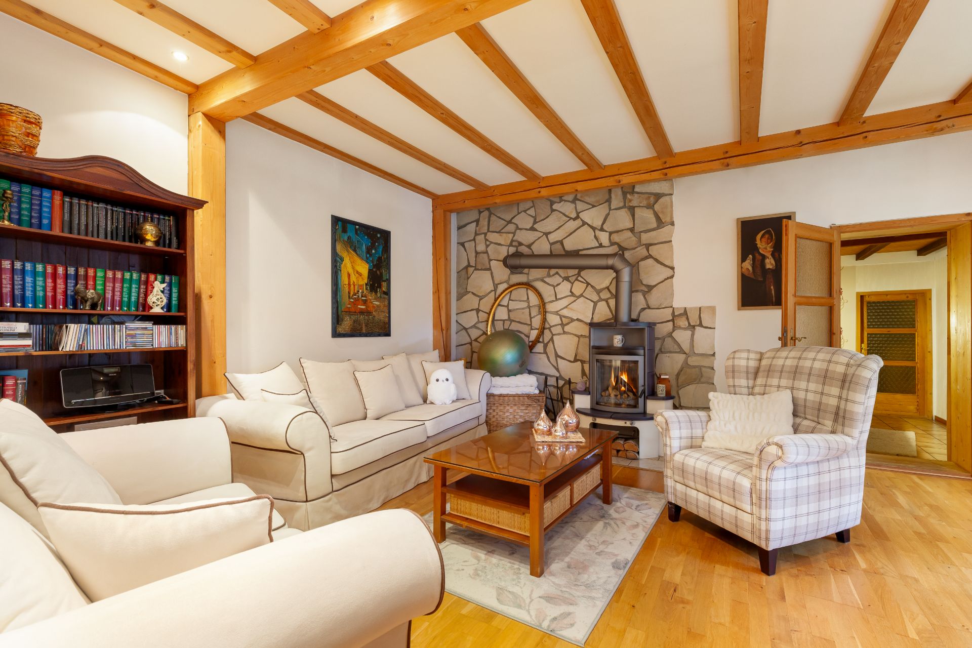 Wohnzimmer mit Kamin, hellen Sofas, Holzdecke und Bücherregal.