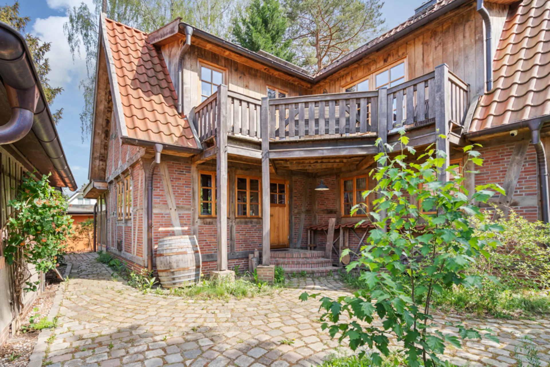 Gemütliches Backsteinhaus mit Holzdetails, Balkon und gepflastertem Innenhof, von Pflanzen umgeben.