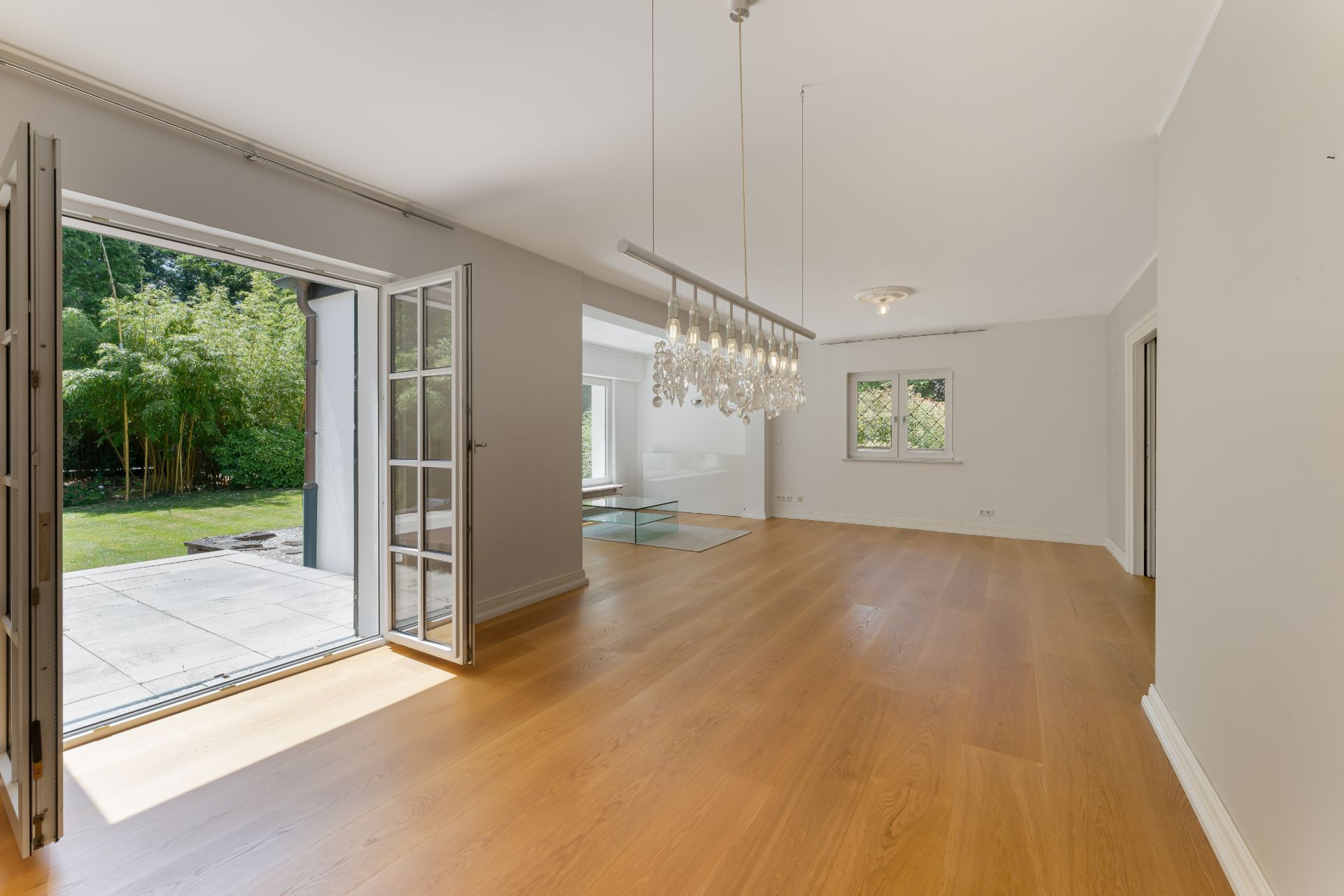 Heller Wohnraum mit Holzboden, großem Fenster und offener Tür zur Terrasse mit Blick auf den Garten.