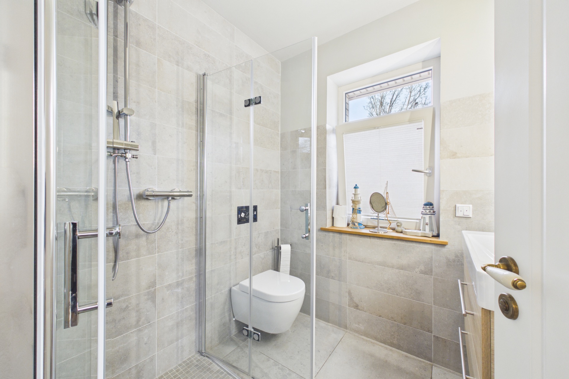 Modernes Bad mit Glasdusche, Wandtoilette und Fenster mit Ablage.