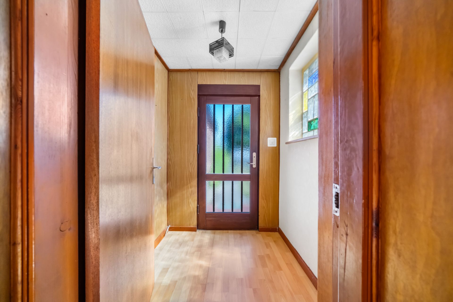Flur mit Holzverkleidung, Holztür mit Glas und Fenster an der Seite.