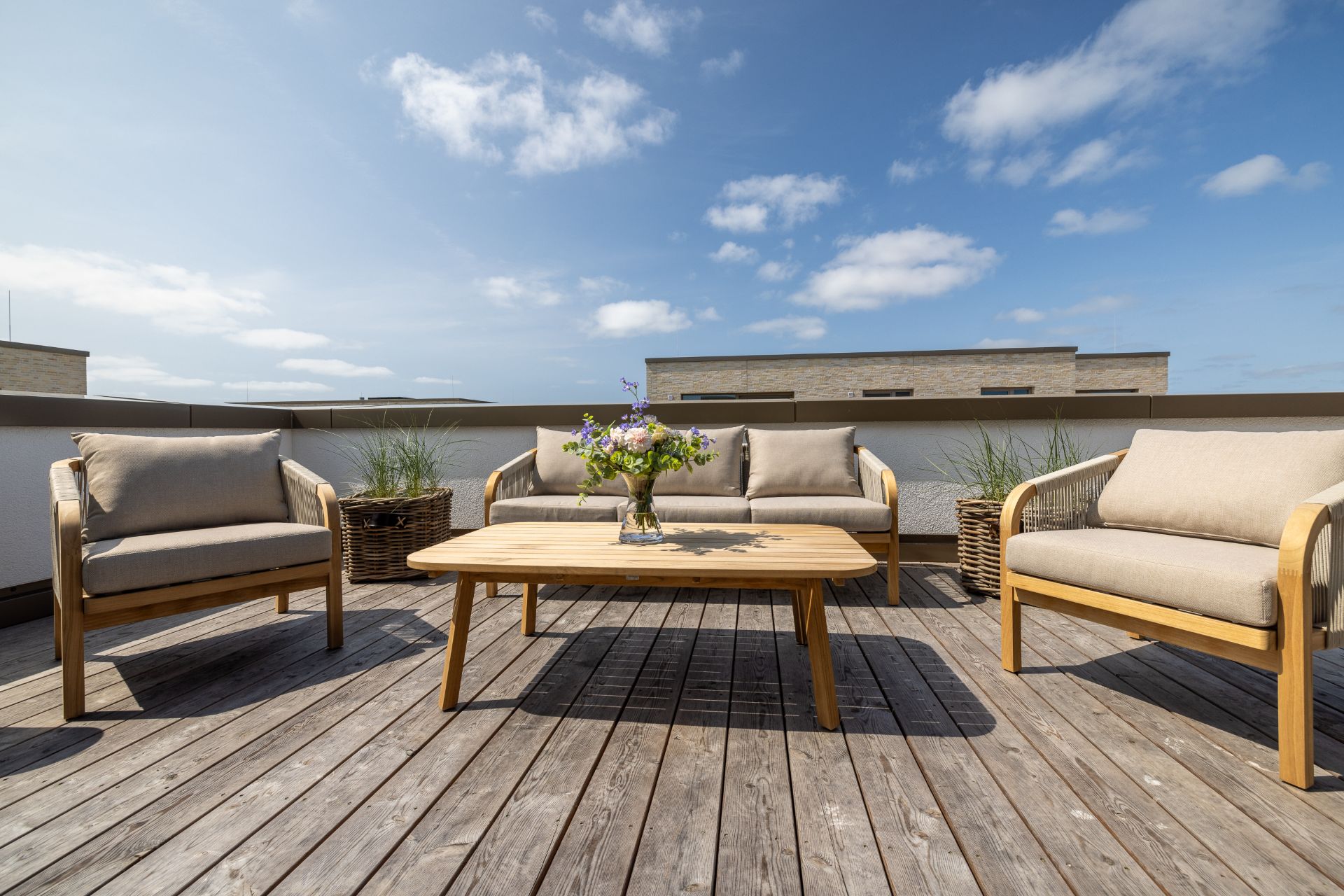 Dachterrasse mit Holzboden, vier Stühlen, Tisch und Blumenvase, Pflanzen im Hintergrund.