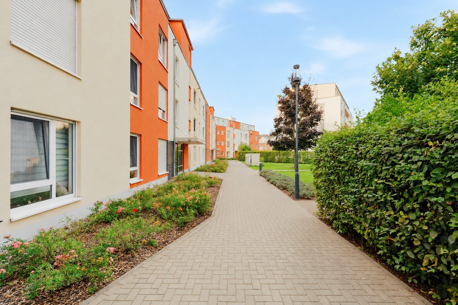 Gepflasterter Weg zwischen modernen Wohngebäuden und grünen Hecken.