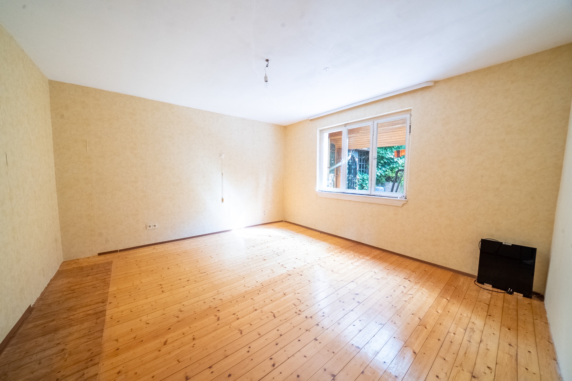 Leerer Raum mit Holzboden, gelben Wänden und großem Fenster.
