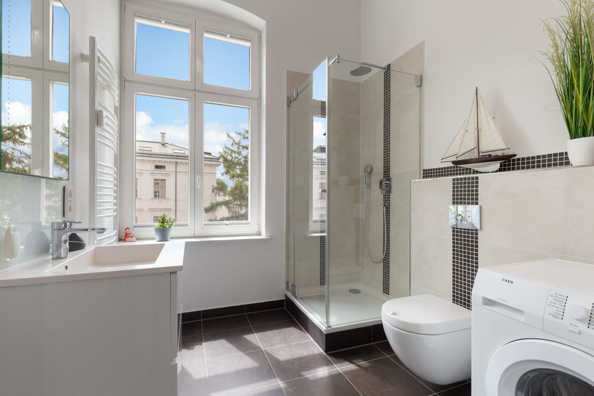 Helles Badezimmer mit Dusche, Toilette, Waschbecken, Waschmaschine und großem Fenster.