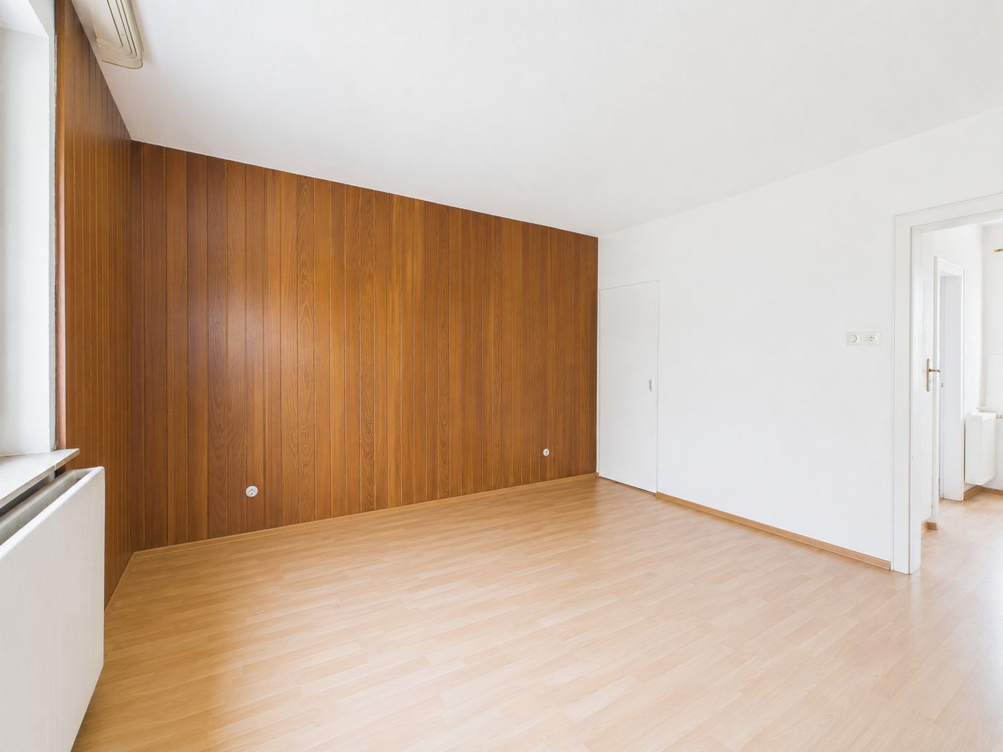 Leerer Raum mit Holzboden und einer Wand aus Holzvertäfelung.