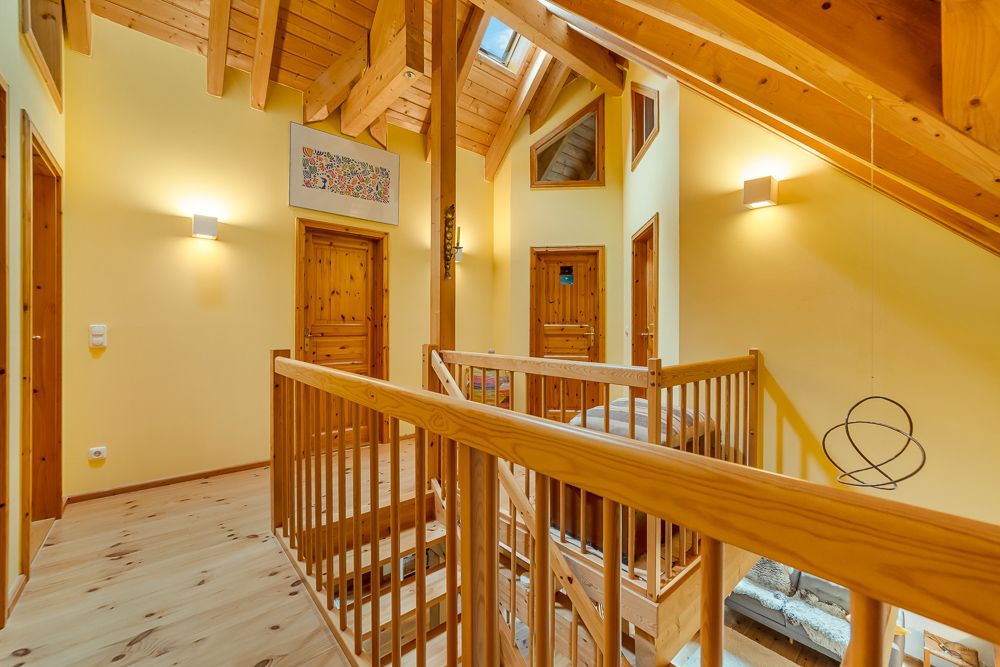 Heller Flur mit Holzbalkendecke, mehreren Türen und Holzgeländer.
