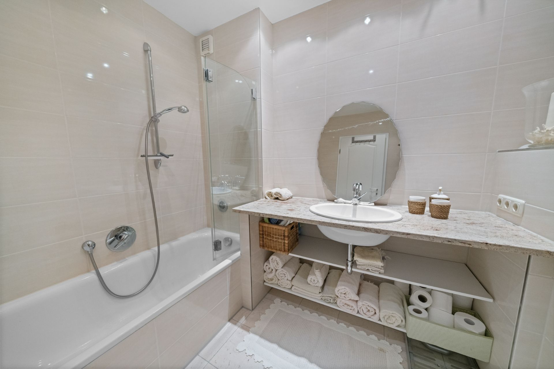 Modernes Badezimmer mit Badewanne, Waschbecken, rundem Spiegel und offenen Regalen mit Handtüchern.