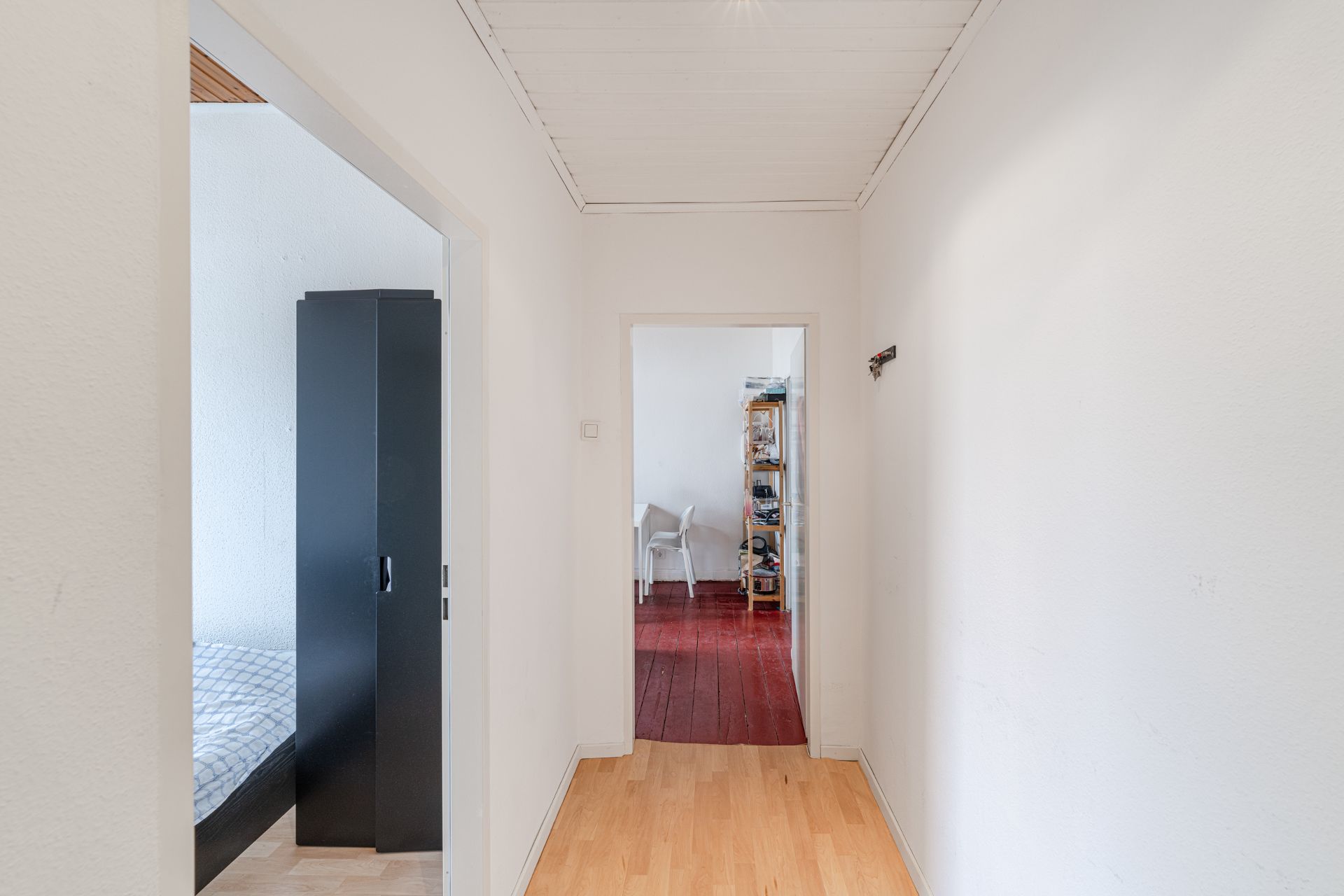 Heller Flur mit Blick in ein Schlafzimmer und ein Zimmer mit Regal und Schreibtisch.