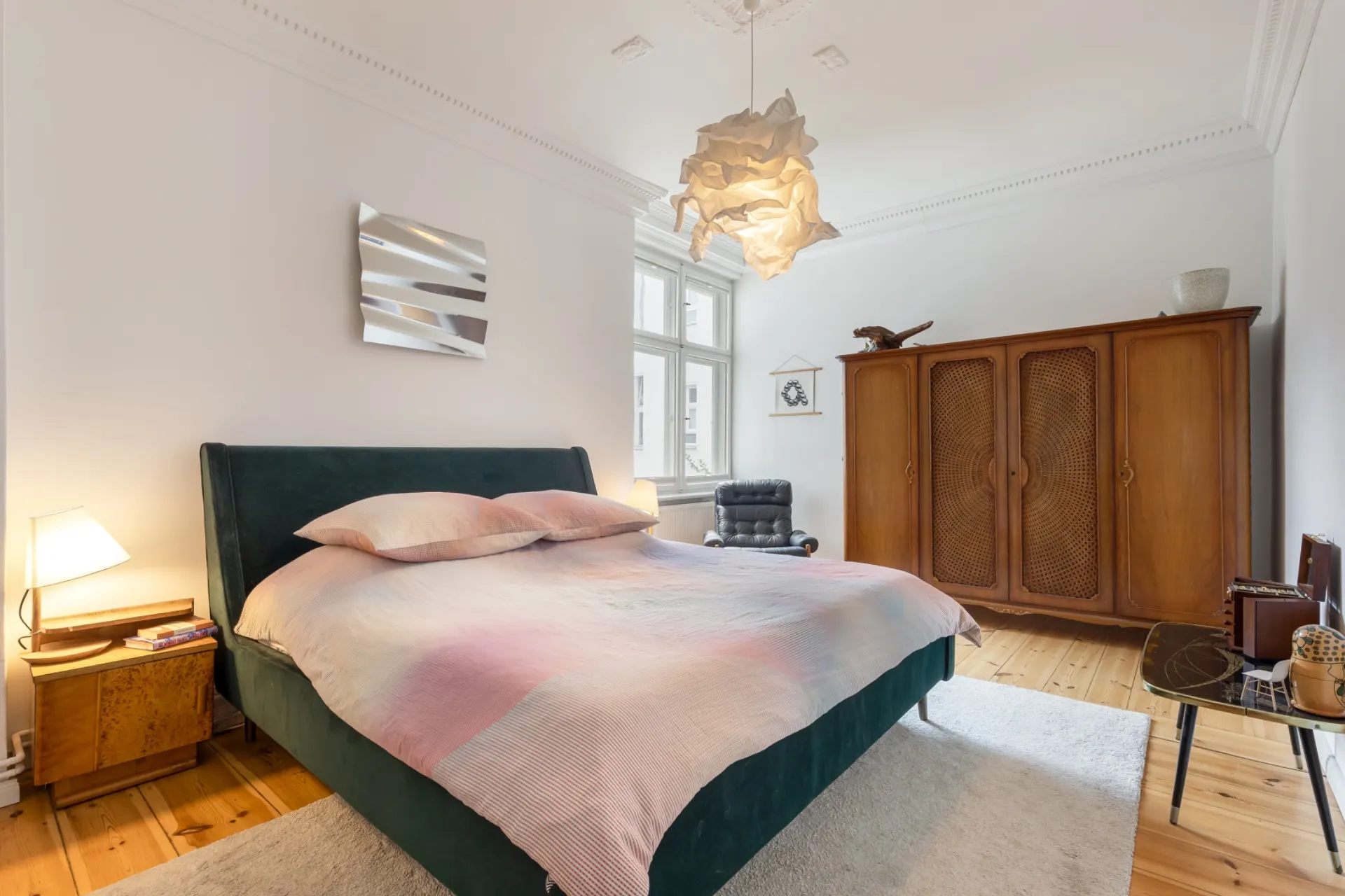 Helles Schlafzimmer mit Doppelbett, Holzschrank, Sessel und großem Fenster.