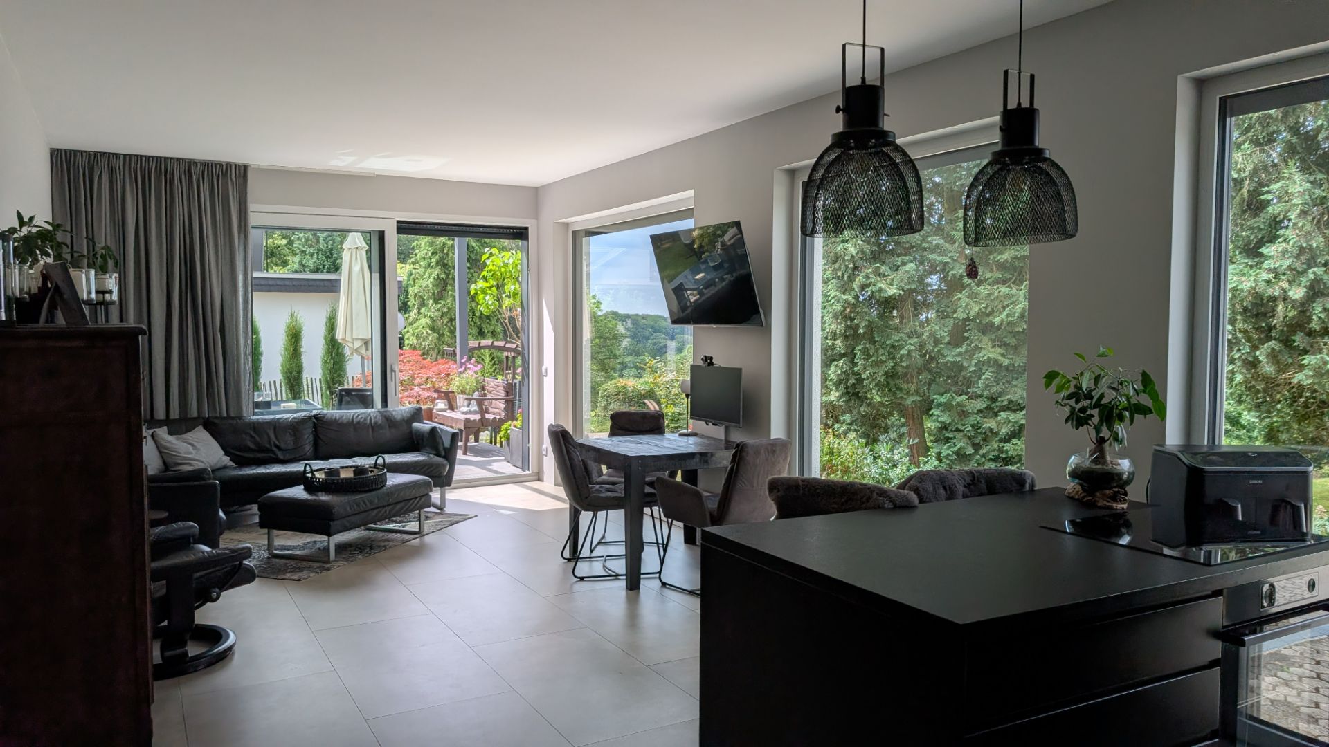 Modernes Wohnzimmer mit Sofa, Essecke, großen Fenstern und Blick auf Terrasse und Garten.