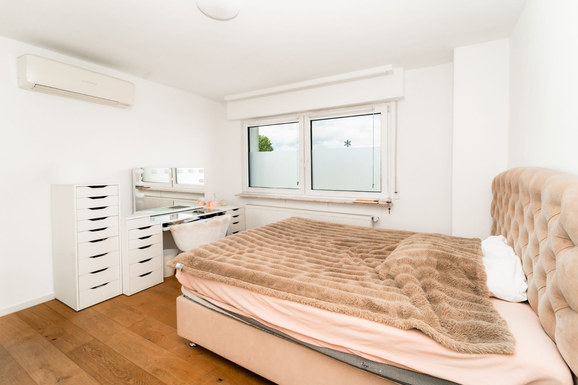 Helles Schlafzimmer mit Doppelbett, Schminktisch und zwei Fenstern.