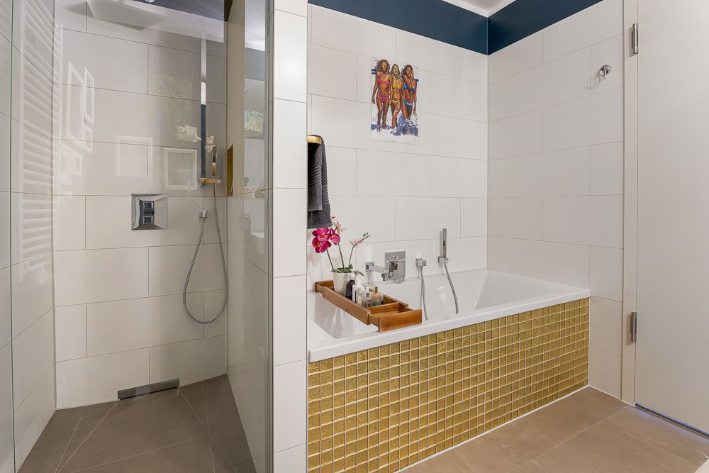 Modernes Badezimmer mit Badewanne, goldenen Fliesen und einer ebenerdigen Dusche.