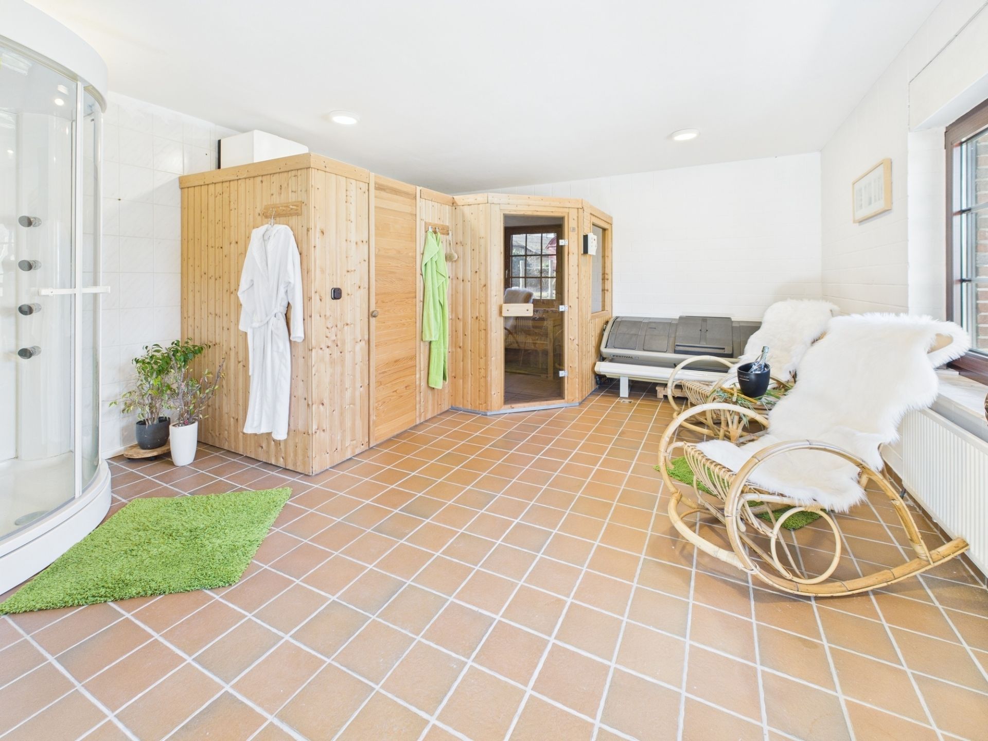 Heller Wellnessraum mit Sauna, Dusche, Liegestühlen und zwei Rattan-Schaukelstühlen mit weißen Auflagen.