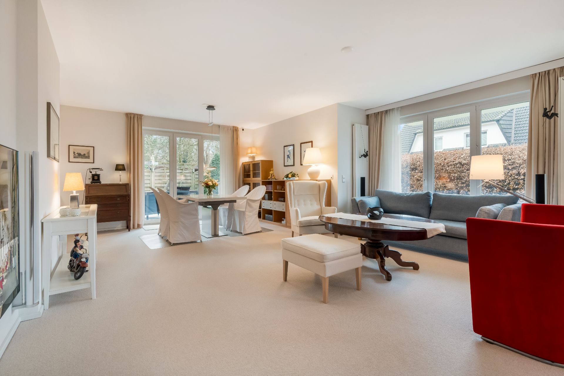 Helles Wohnzimmer mit Sofa, Esstisch, Sesseln und großen Fenstern mit Blick nach draußen.