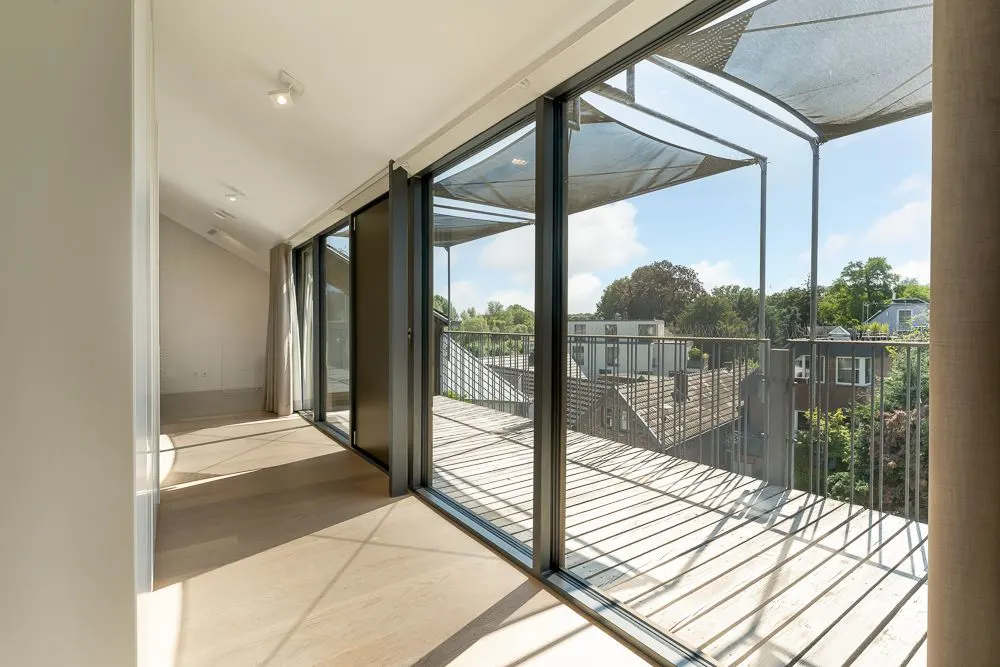 Helles Zimmer mit großen Glas-Schiebetüren und Zugang zu einem Balkon mit Blick ins Grüne.