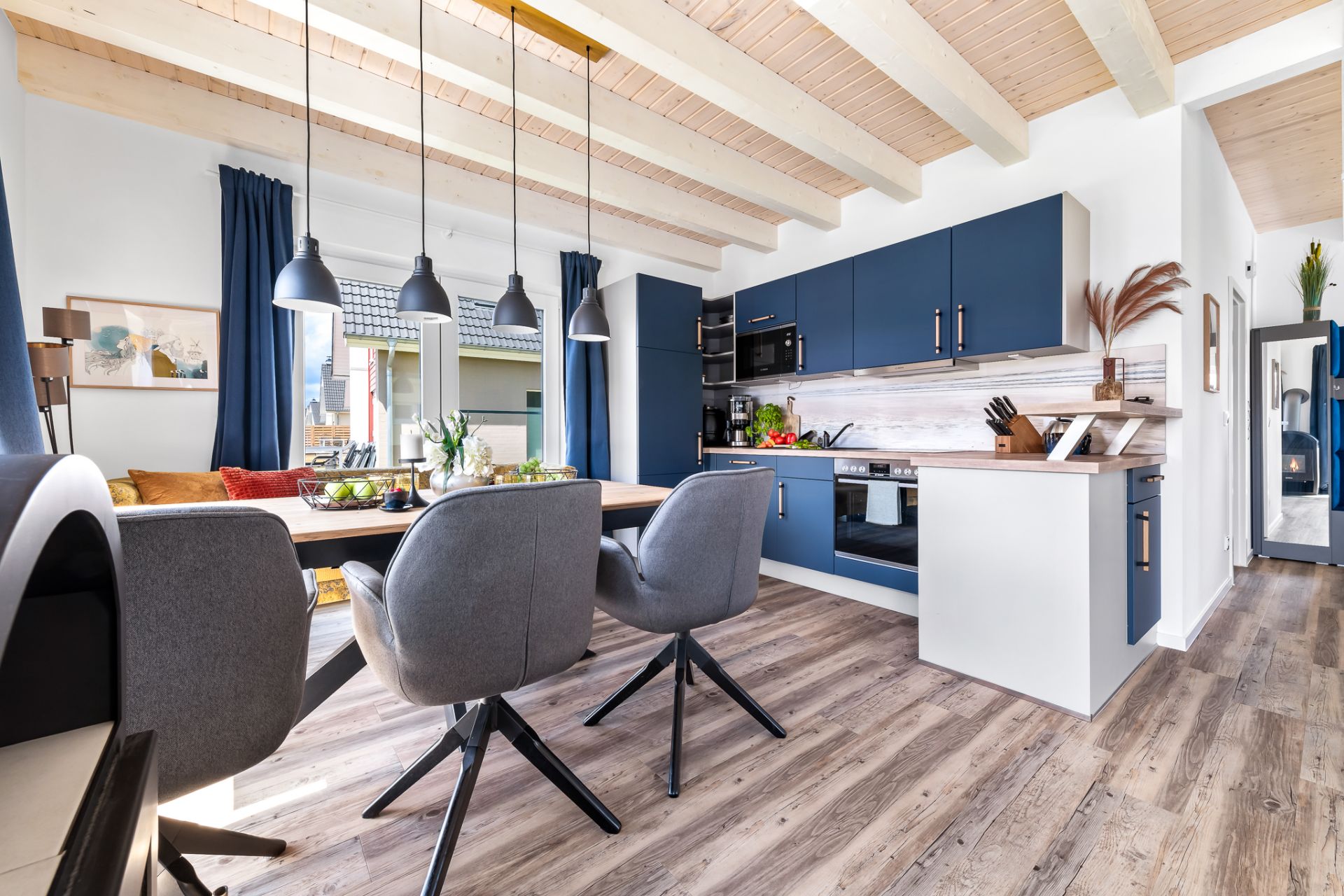 Moderne offene Küche mit blauen Schränken, Essbereich und Holzbalkendecke.