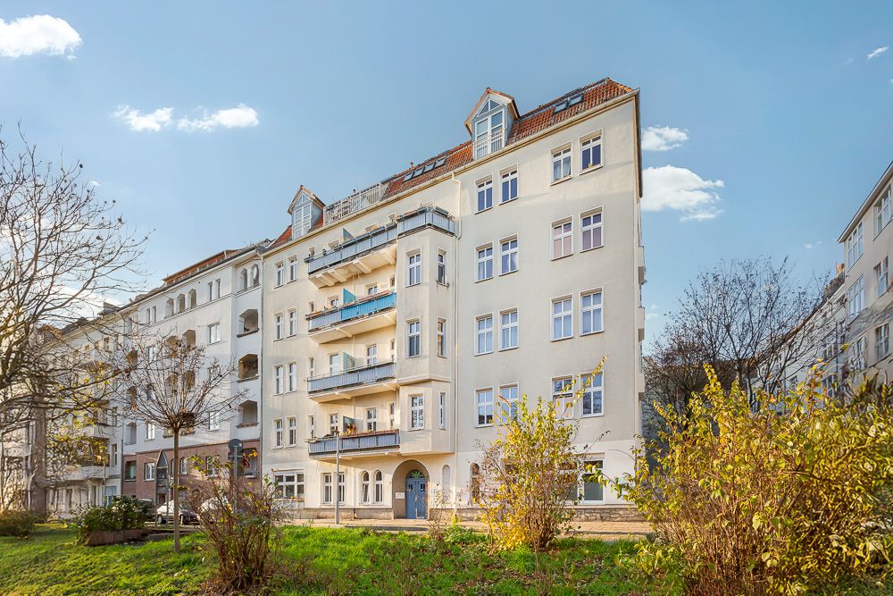 Mehrstöckiges Wohnhaus mit Balkonen, davor grüner Vorgarten und Büsche.