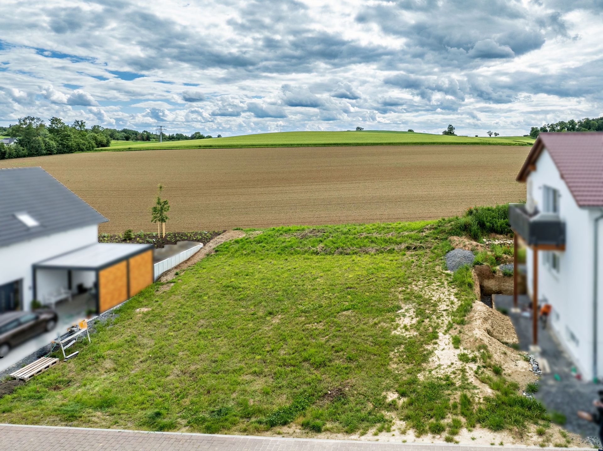 Unbebaute Wiese zwischen zwei Wohnhäusern mit Blick auf ein Feld.