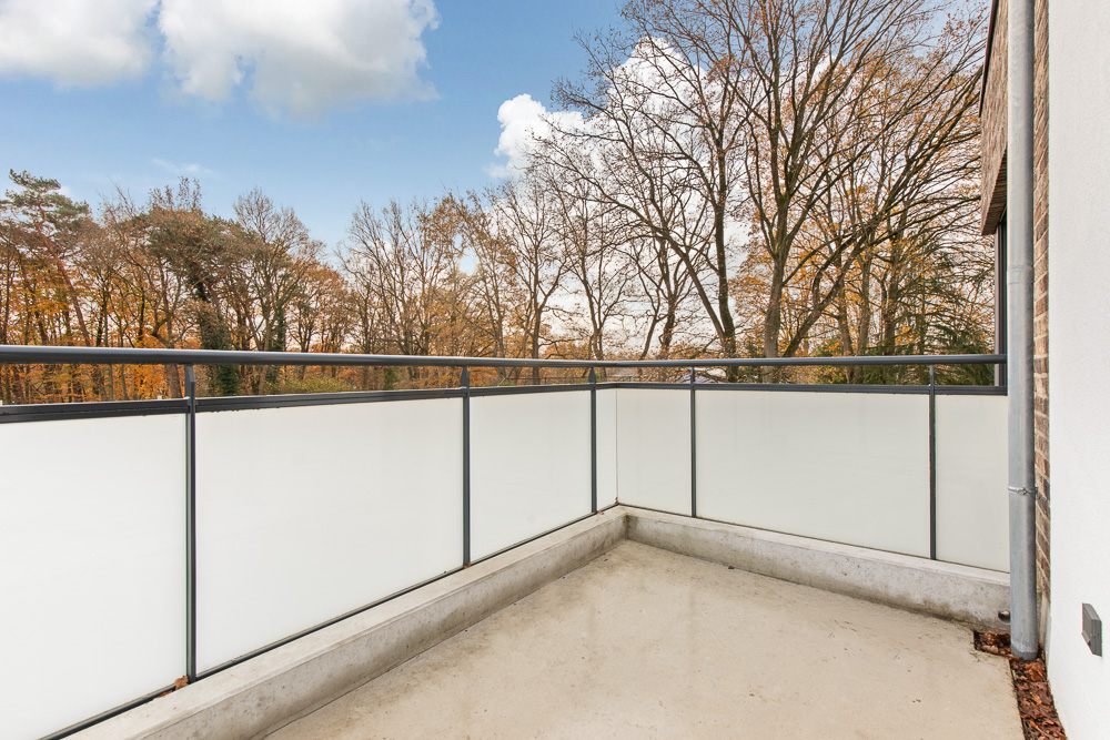 Moderner Balkon mit Milchglasgeländer, Ausblick auf Bäume im Herbst.