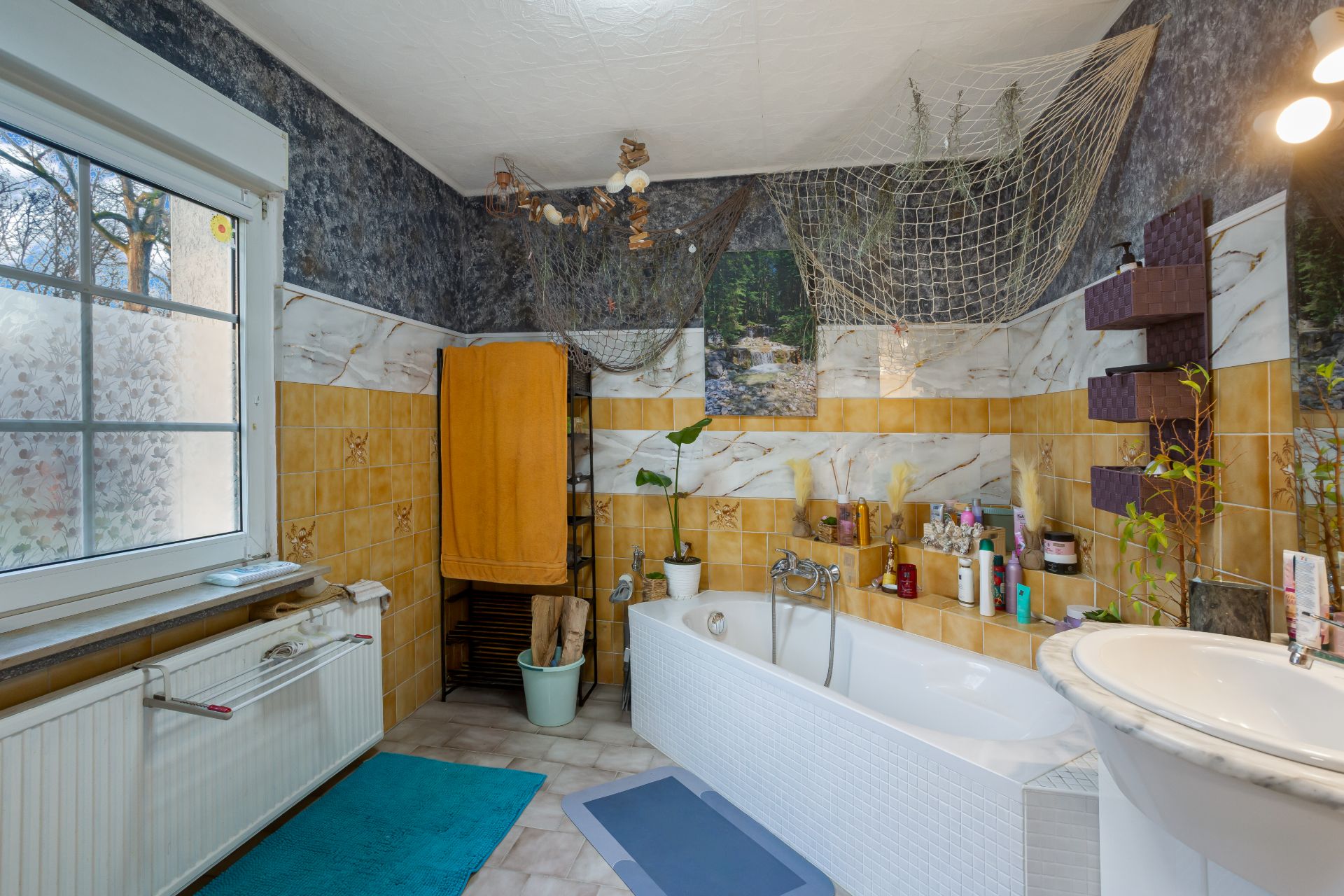 Helles Badezimmer mit Badewanne, Waschbecken, Pflanzen und Dekor an der Wand.