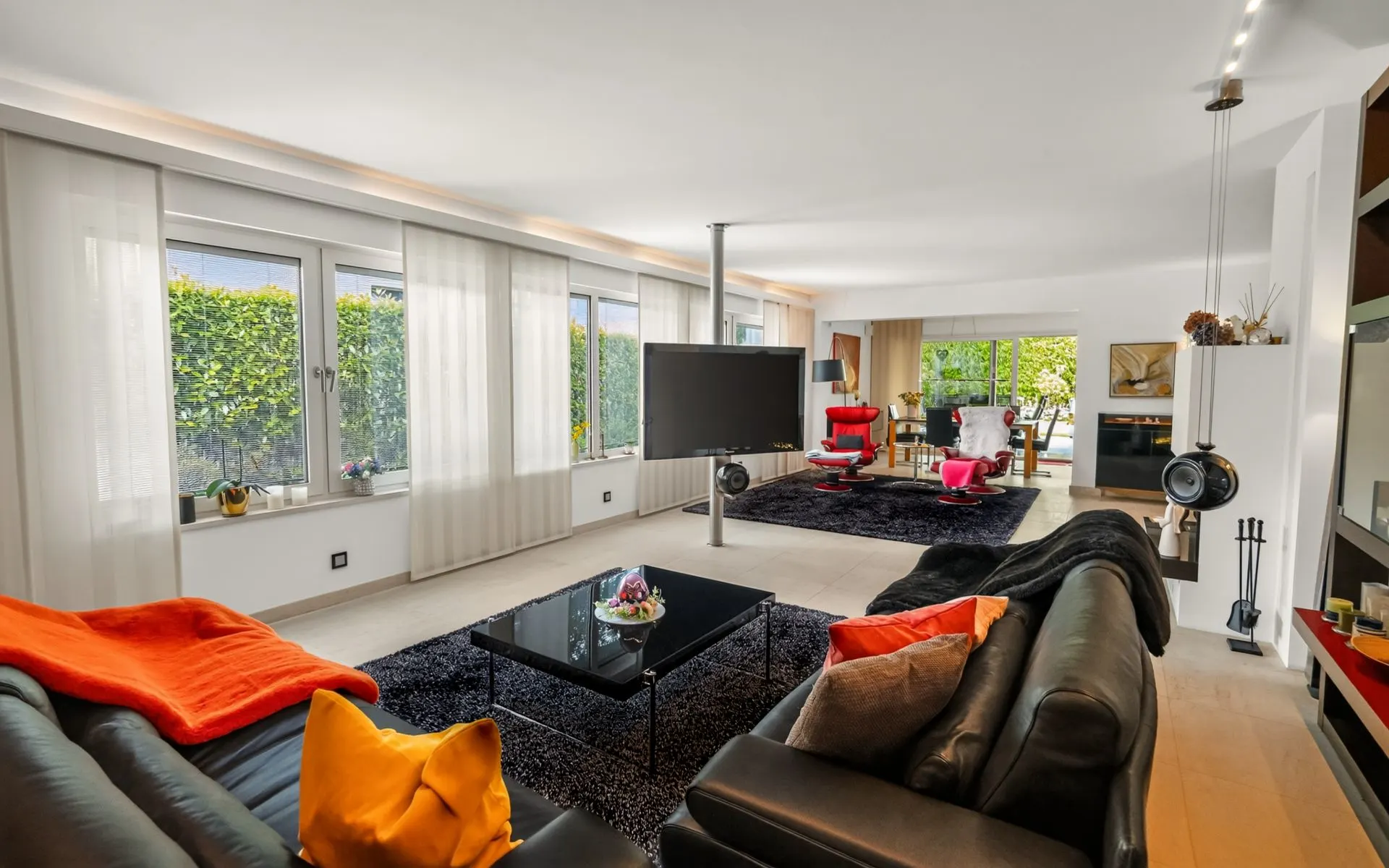 Modernes Wohnzimmer mit großen Fenstern, schwarzen Sofas, TV und farbigen Kissen.