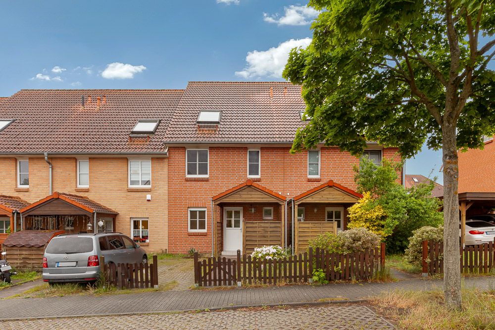 Zweistöckiges Reihenhaus aus Backstein mit Vorgarten, Holzzaun und einem geparkten Auto davor.