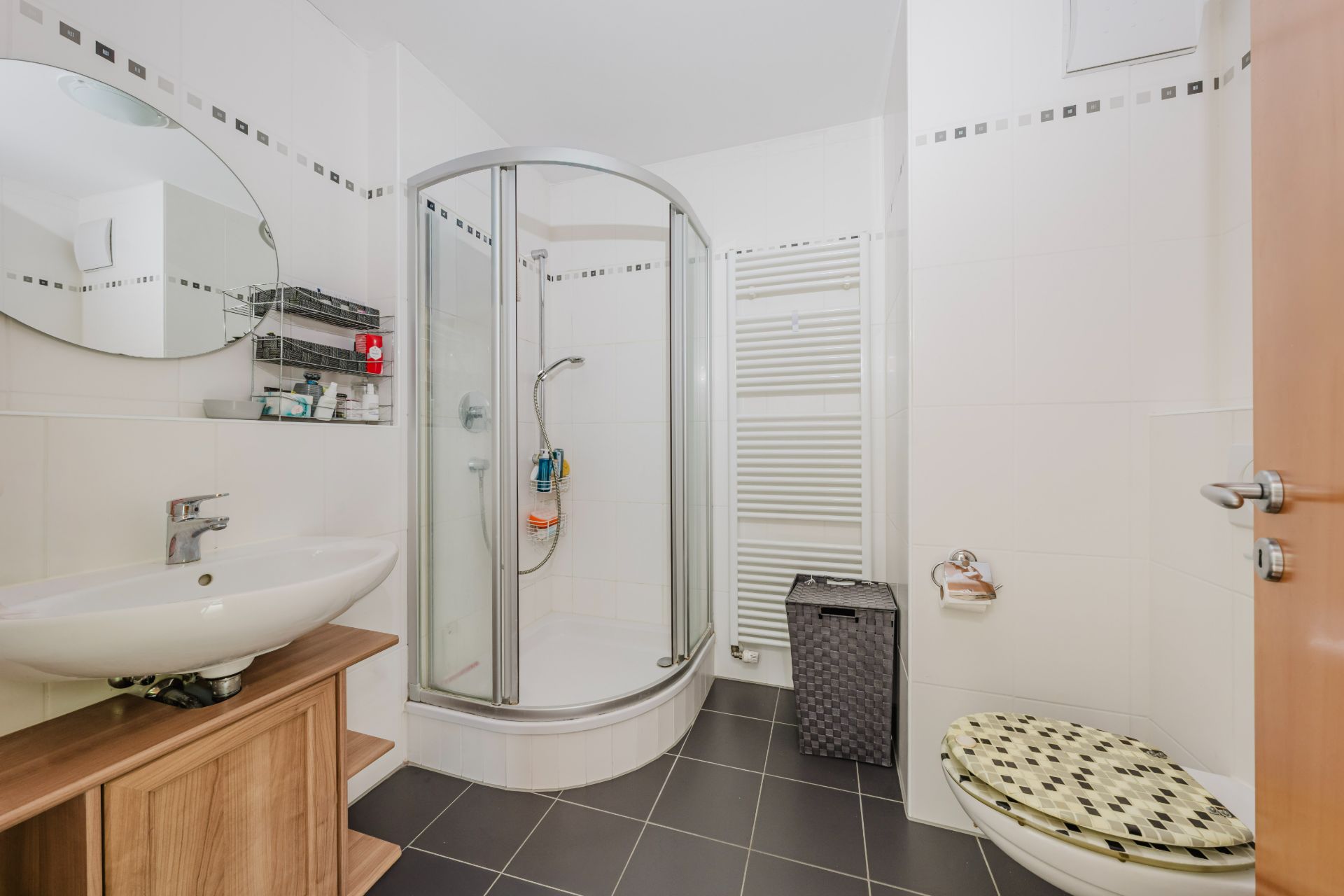 Modernes Badezimmer mit Dusche, Waschbecken, Spiegel, WC und Heizkörper.