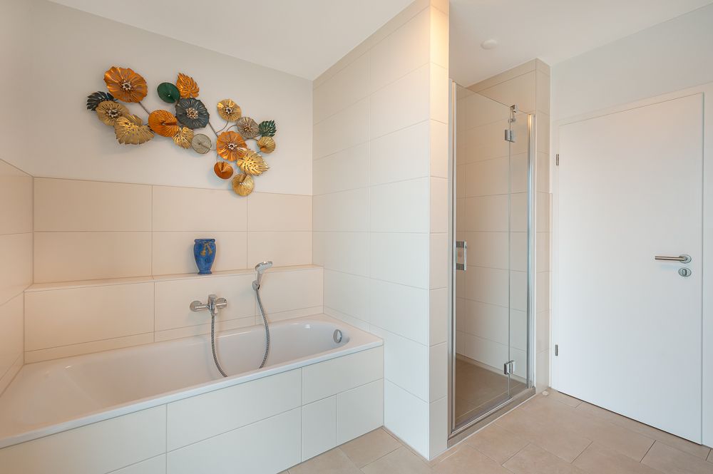 Modernes Bad mit Badewanne, Dusche und bunter Wanddeko über der Wanne.