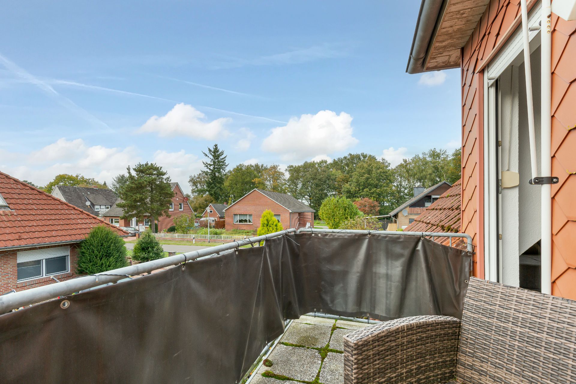 Balkon mit Blick auf Wohnhäuser und Bäume, ein Stuhl steht auf dem Balkon.