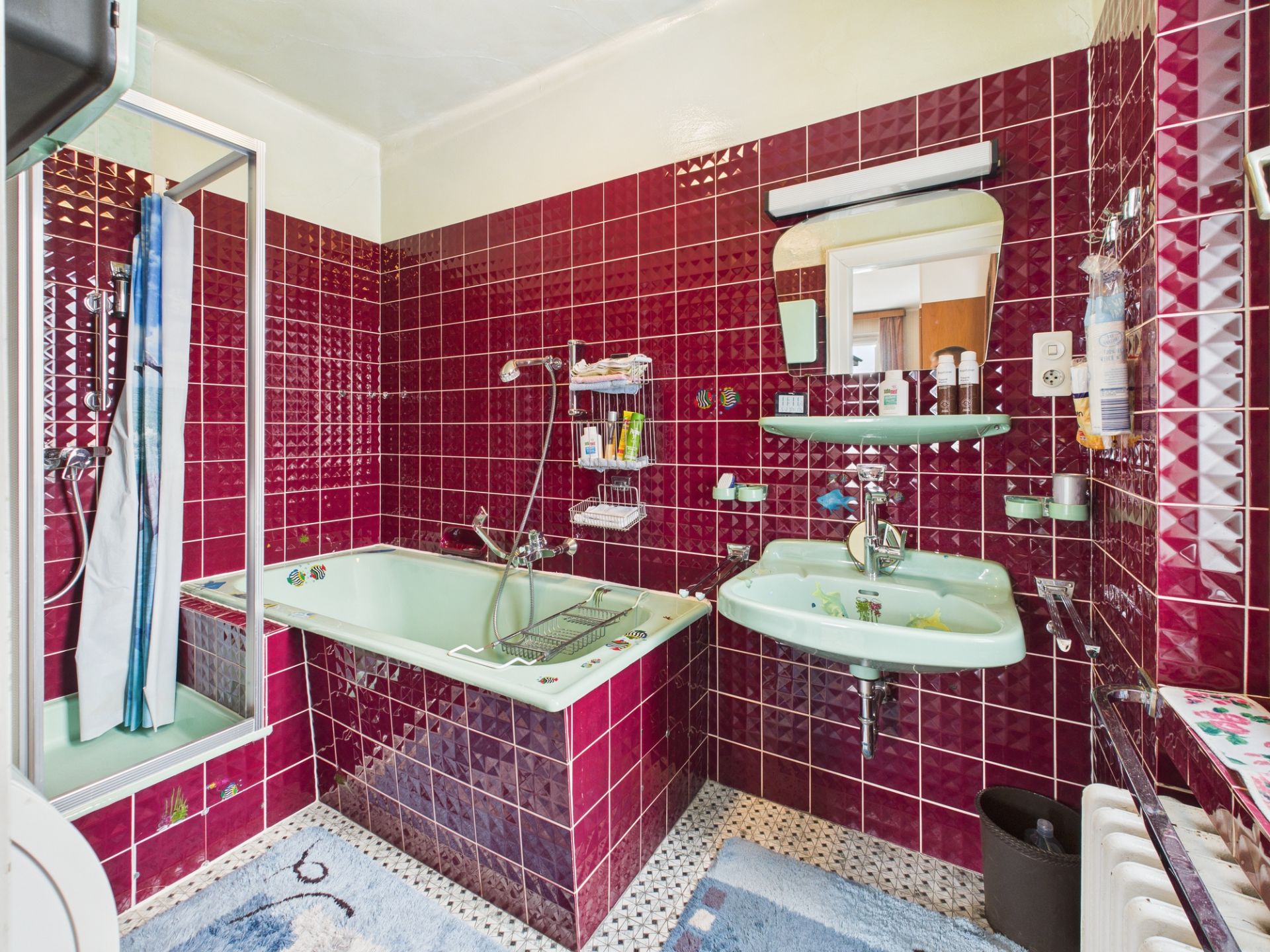 Badezimmer mit grünen Sanitäranlagen, roter Fliesenwand, Badewanne, Dusche und Waschbecken.