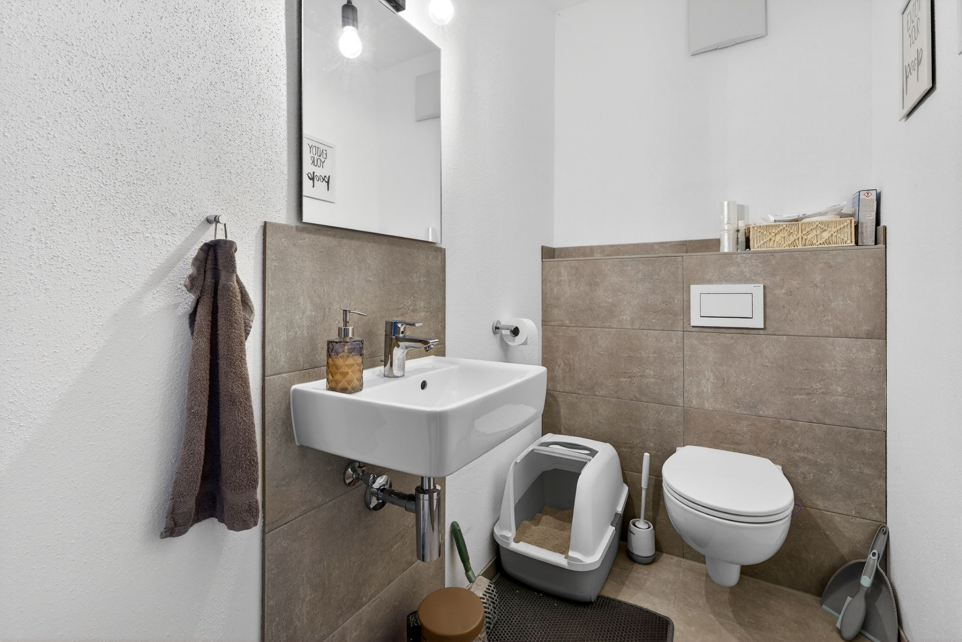 Modernes Bad mit Waschbecken, Wandtoilette, Katzenklo und Handtuch an der Wand.