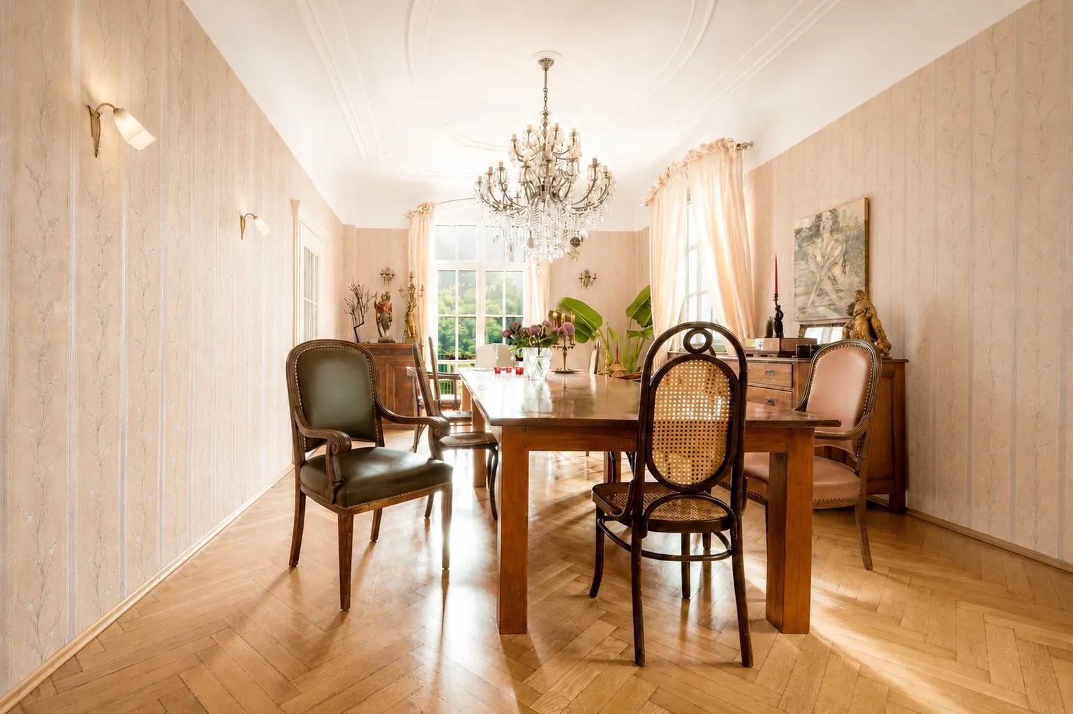 Heller Essbereich mit Holztisch, Stühlen, Kronleuchter und großen Fenstern.