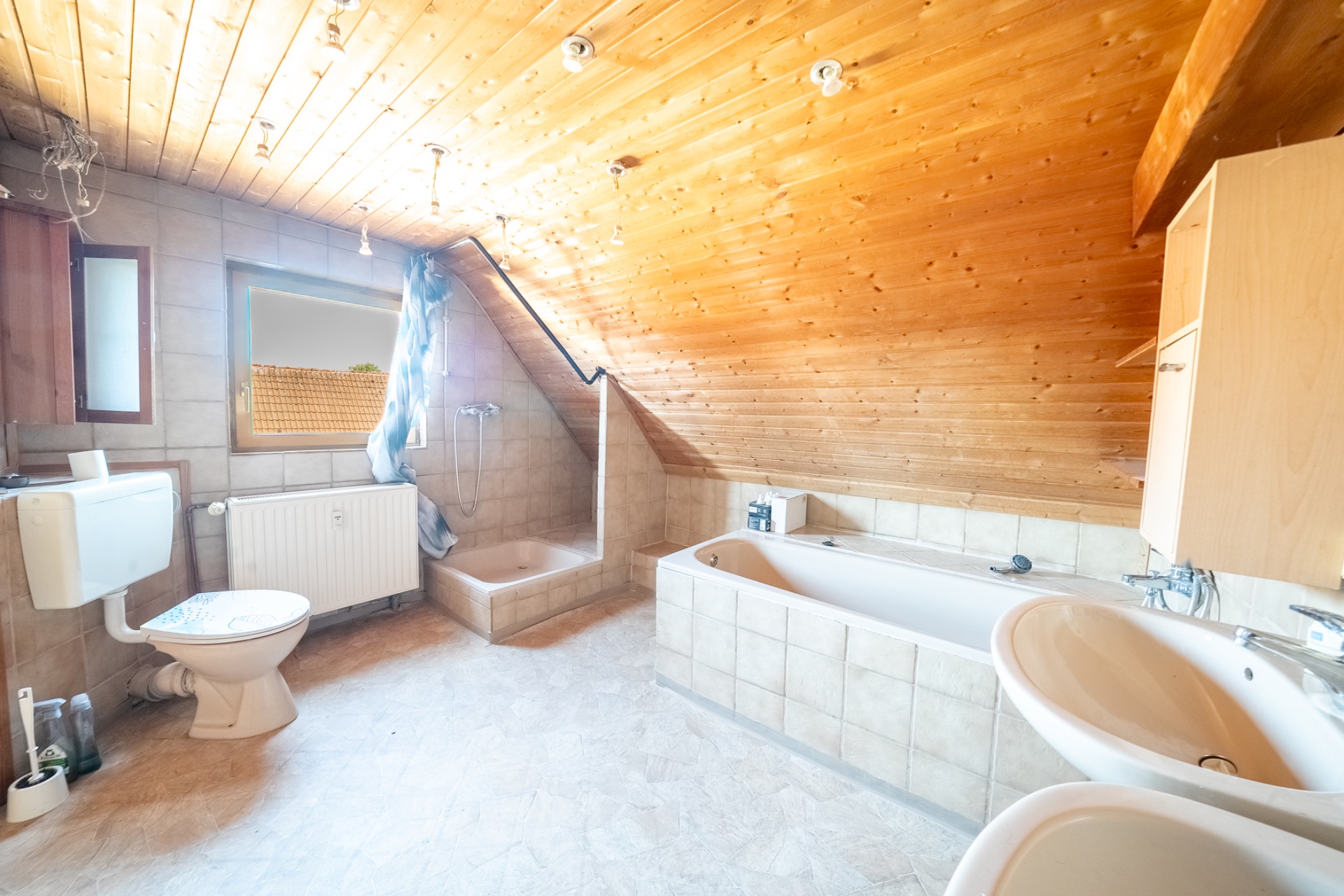 Helles Bad mit Dachschräge, Badewanne, Dusche, Toilette, Waschbecken und Holzwanddecke.