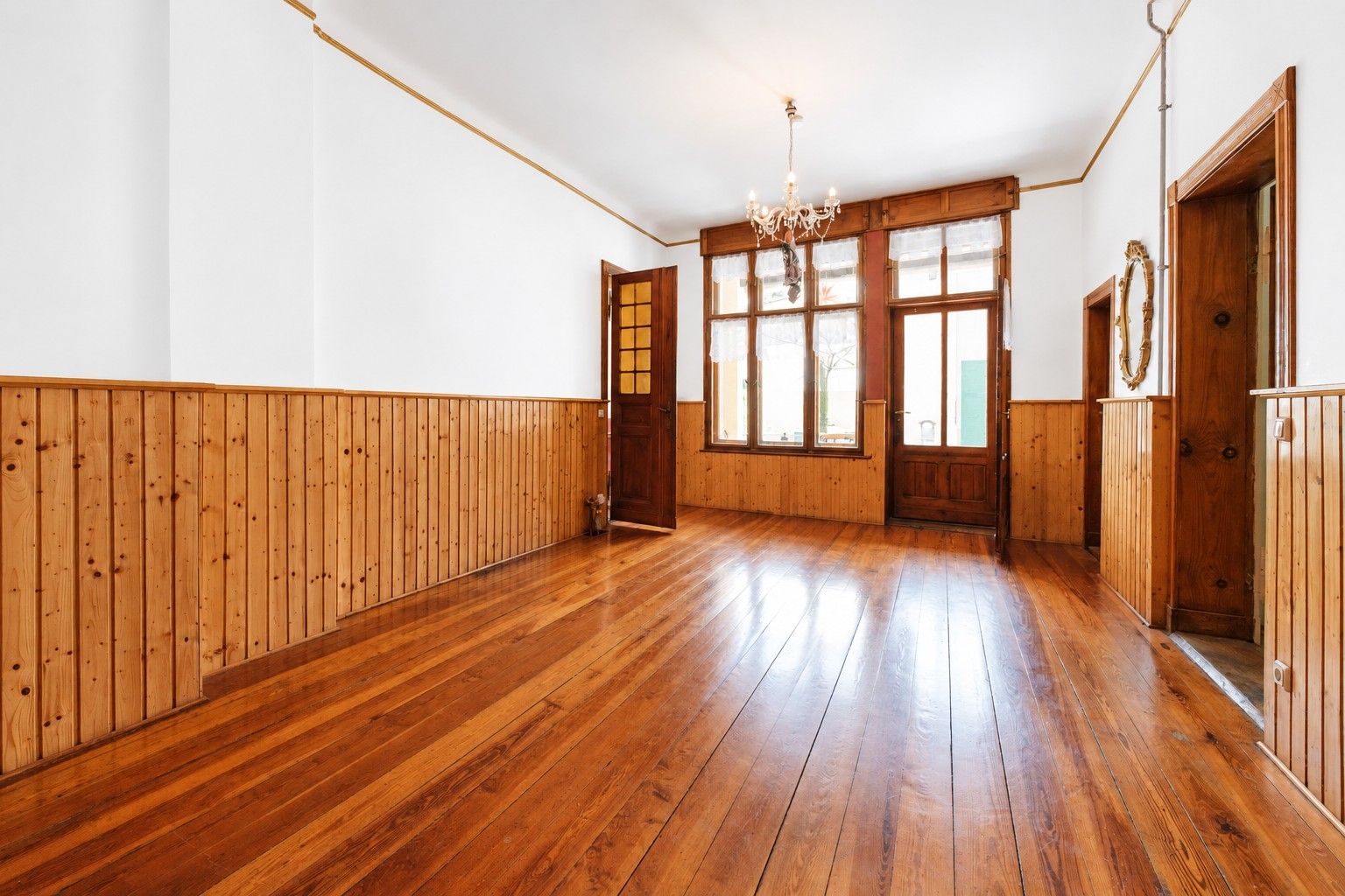 Leerer Raum mit Holzfußboden, Holzvertäfelung und großem Fenster mit Glastür.