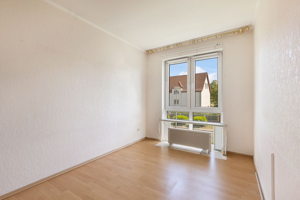 Leerer, heller Raum mit Holzboden und großem Fenster, Blick auf Nachbarhaus.