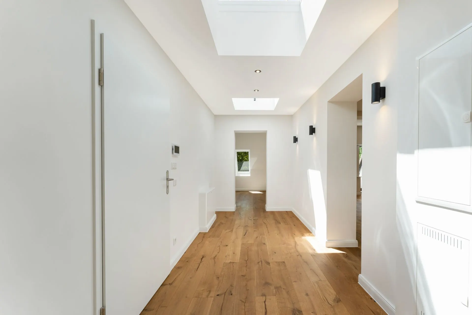 Heller Flur mit Holzboden, weißen Wänden und Oberlichtern in einem Wohnhaus.