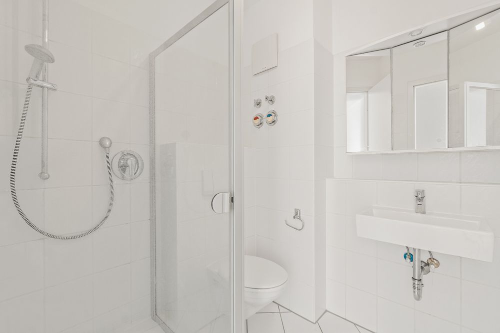 Helles Bad mit Dusche, WC, Waschbecken und Spiegelschrank.