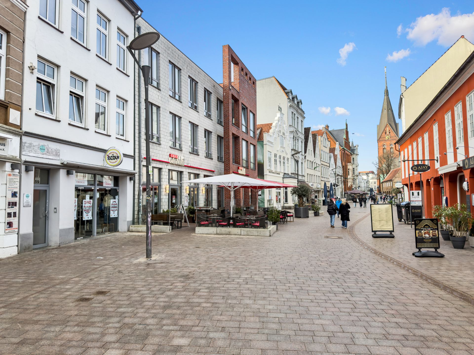 Fußgängerzone mit Geschäften, Cafés und Menschen, die die Straße entlanggehen.