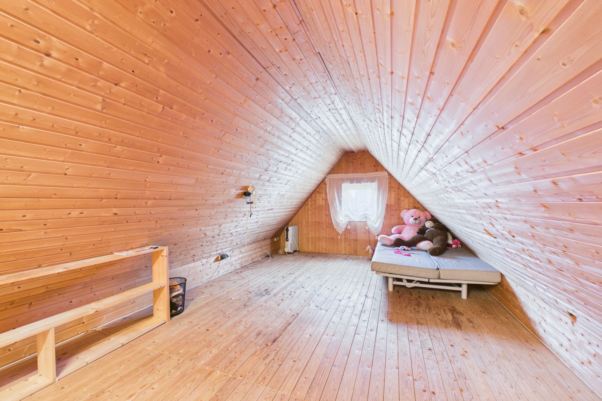 Dachzimmer mit Holzverkleidung, Matratze am Fenster und zwei großen Teddybären.
