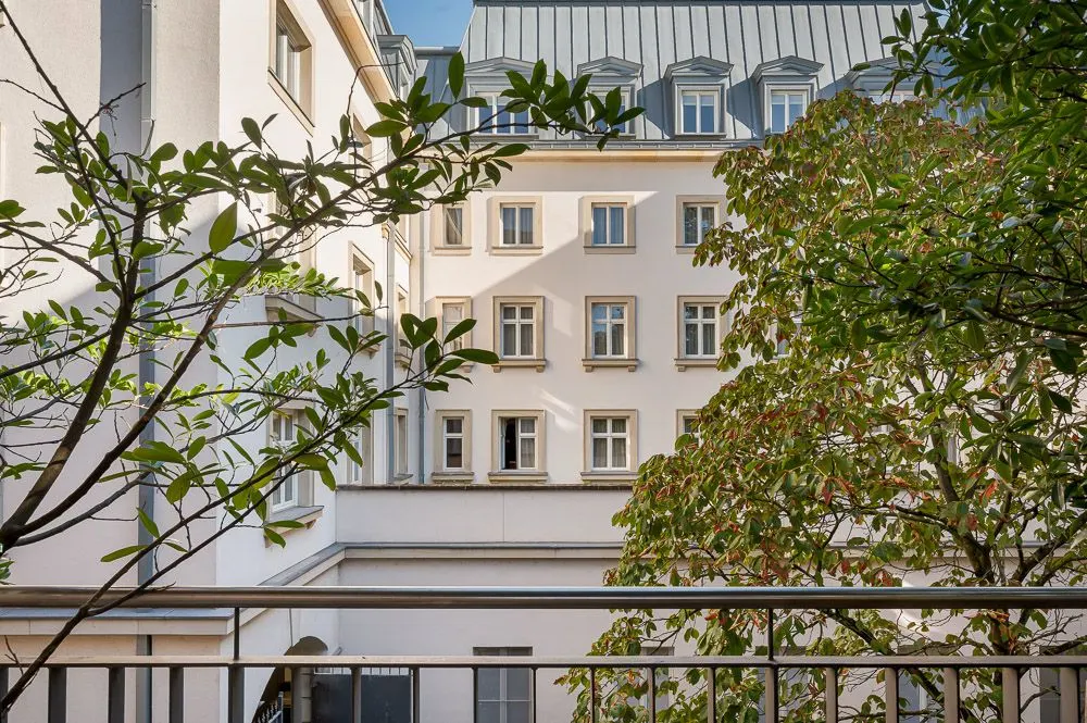 Blick von einem Balkon auf ein Wohngebäude mit Bäumen im Vordergrund.